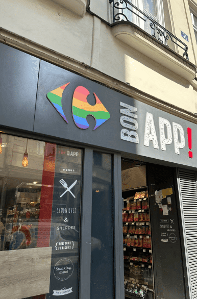 Enseigne Carrefour arc-en-ciel en façade d'un magasin Bon App ! Depuis trois ans, Carrefour s’engage à soutenir la communauté LGBT au sein de l’entreprise et s’associe, cette année, à la Fondation Le Refuge pour aider matériellement et accompagner vers l’emploi les jeunes LGBT en situation d’exclusion.