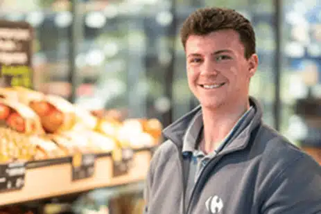 Collaborateur souriant, devant un rayon de fruits et légumes