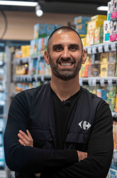 Franchisé Carrefour, souriant, devant les rayons de son magasin