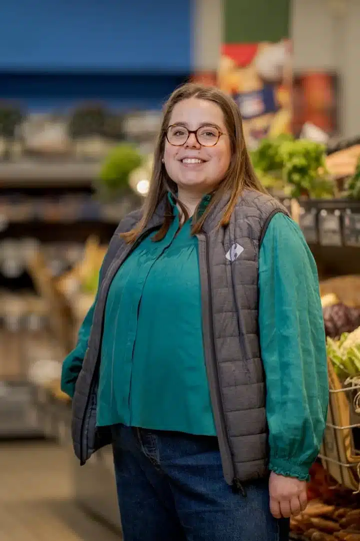 Collaboratrice Carrefour souriante devant un rayon de fruits et légumes