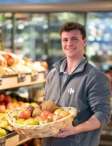 Collaborateur souriant, devant un rayon de fruits et légumes