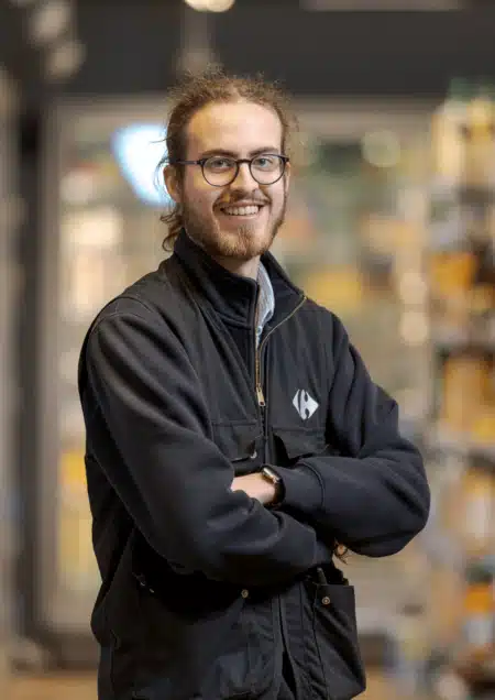Collaborateur Carrefour souriant, devant un rayon de fruits et légumes